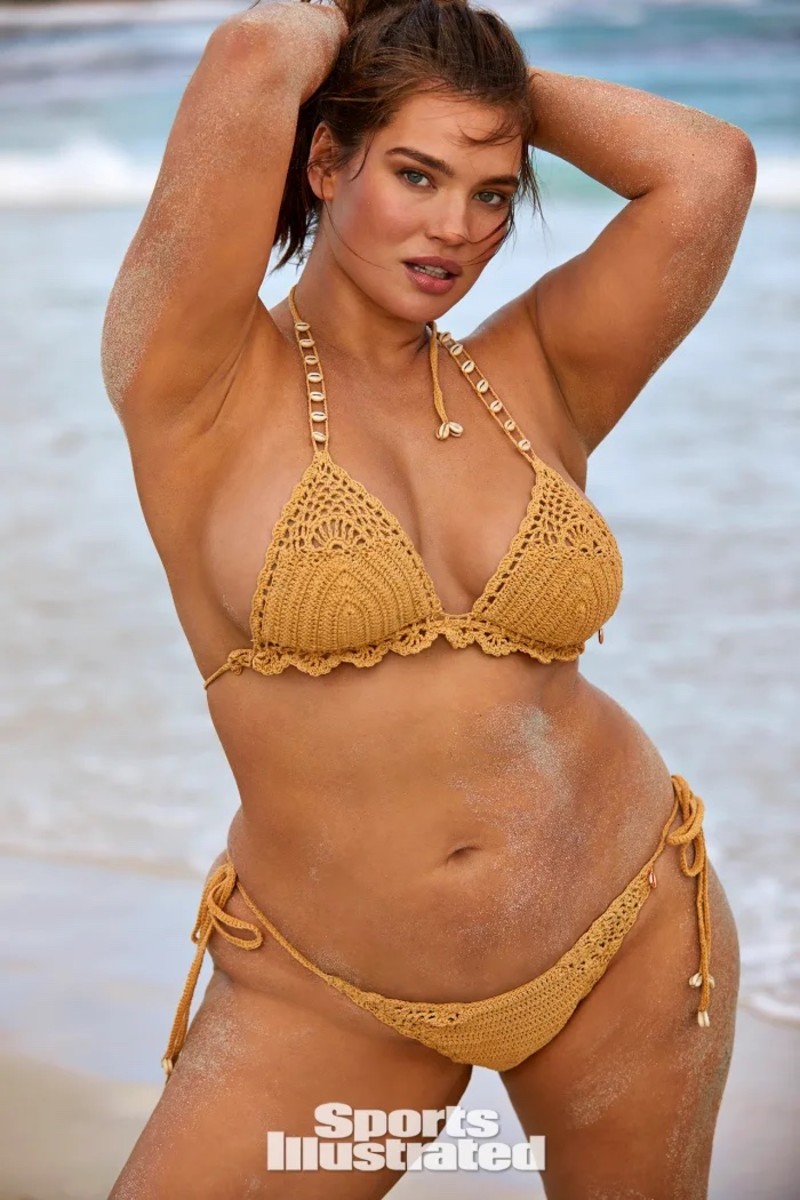 Tara Lynn poses with her arms above her head in a tan crocheted bikini.
