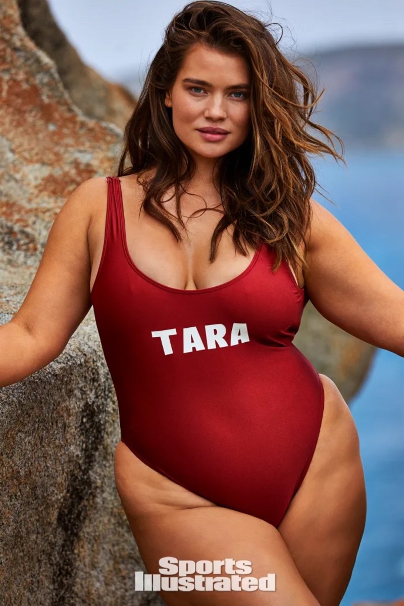 Tara Lynn poses in front of the rocks in a red one-piece with her name written on it.