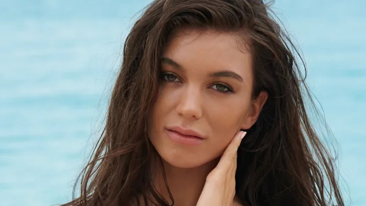 Erin Willerton poses in front of the ocean and looks at the camera.