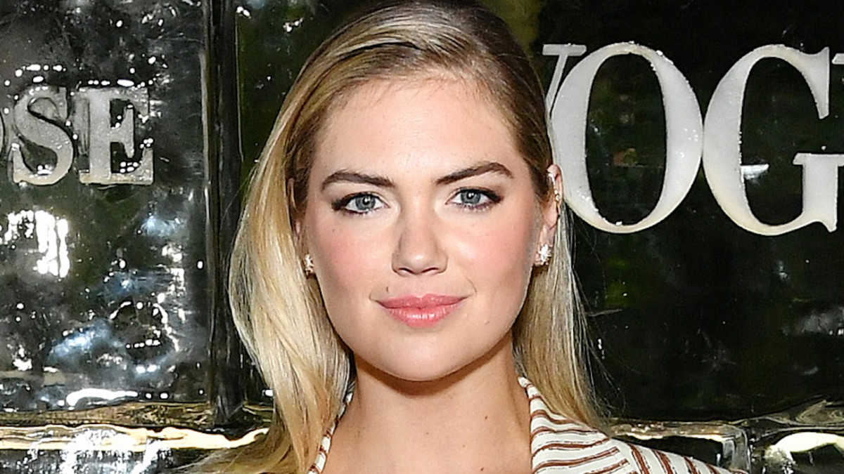 Kate Upton poses in a striped blazer and diamond earrings and smiles for the camera.