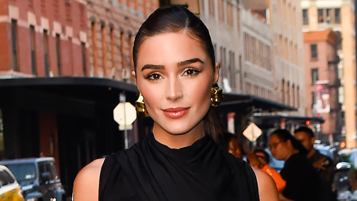 Olivia Culpo poses in a high-neck black top and oversized gold hoops.