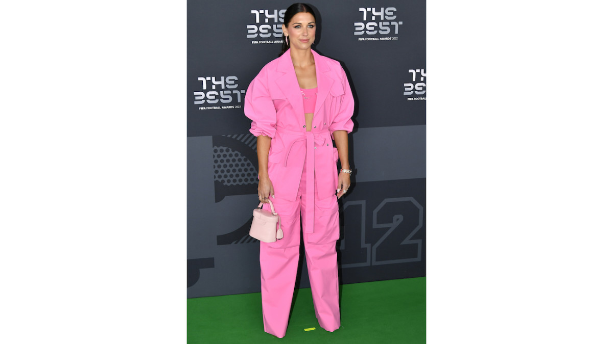 Alex Morgan poses on a red carpet in a hot pink suit and bralette.