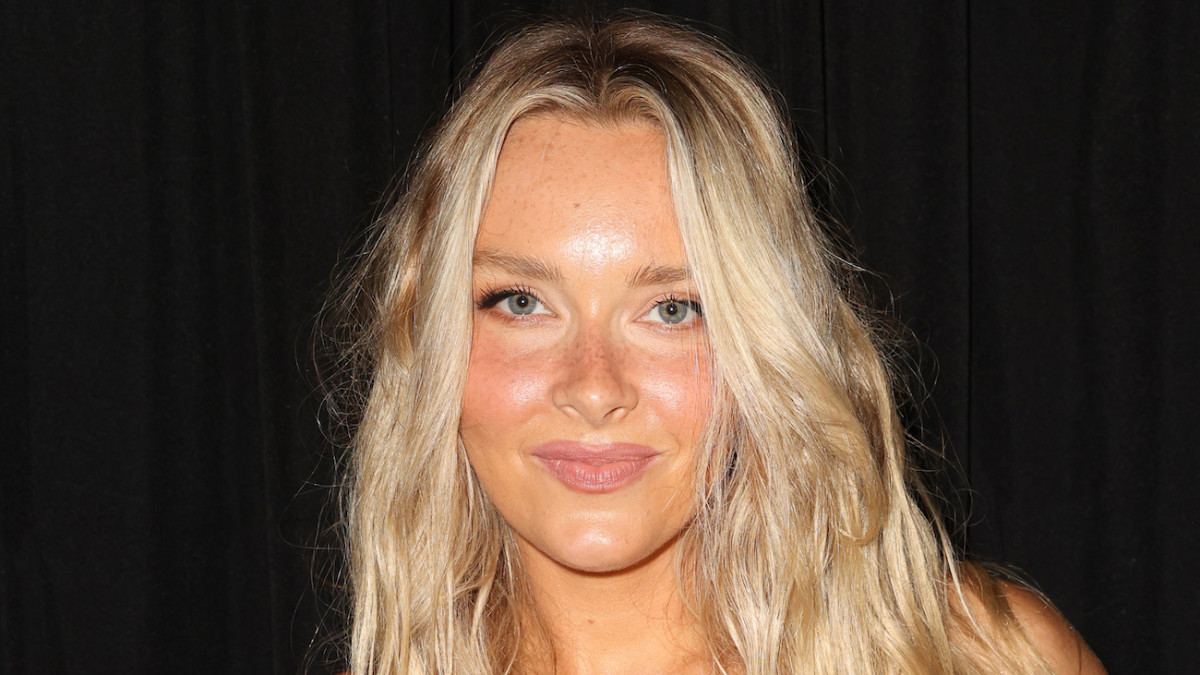 Camille Kostek sports her blonde hair in a soft wave and smiles for the camera.