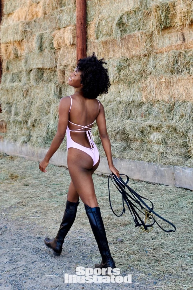 Tanaye White walks through a field in a pink tie-back one-piece and black leather boots.