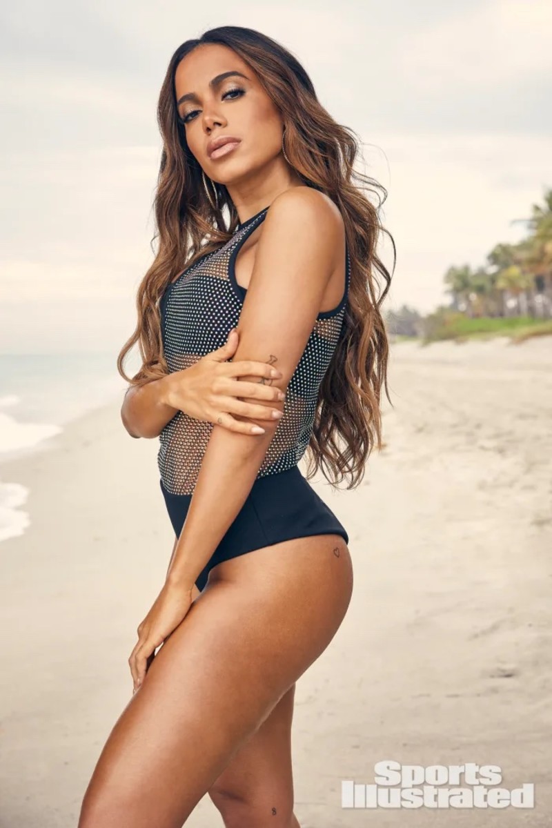 Anitta stands on the sand in a black sequined one-piece.