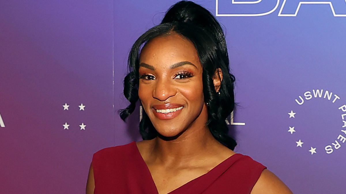 Crystal Dunn poses in a deep berry-colored V-neck top and a messy up-do and smiles for the camera.