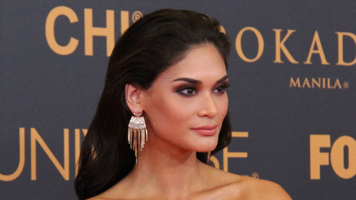 Pia Wurtzbach wears metallic drop earrings, moody eye makeup and sports her black hair in a blow out and looks off into the distance.