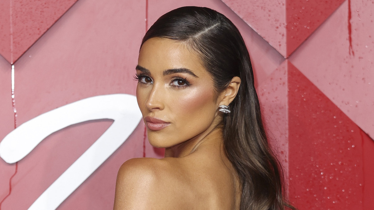 Olivia Culpo poses in a strapless dress and slicked-back up-do and looks over her shoulder at the camera.