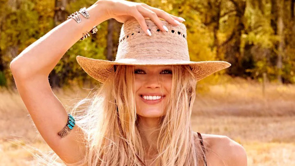 Vita Sidorkina poses with her hand resting on her straw hat and smiles for the camera.