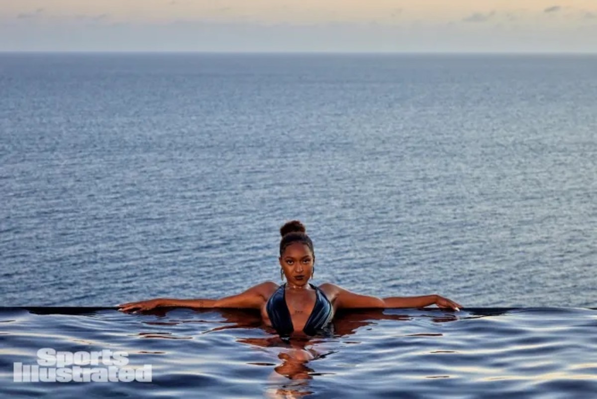 DiDi Richards lounges in a pool in front of the ocean in a one-piece swimsuit.